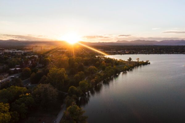Aerial view of Denver, Colorado at dusk with large lake and sun setting behind the foothills.