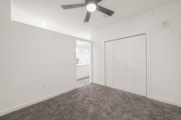 29x apartment bedroom with plush carpet, large closet, and ceiling fan.