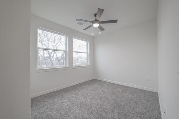 29x apartment bedroom with plush carpet, large windows, and ceiling fan.