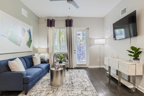 500 Ocean apartment living room with wood style floor, plush seating, wall mounted TV, and balcony door.