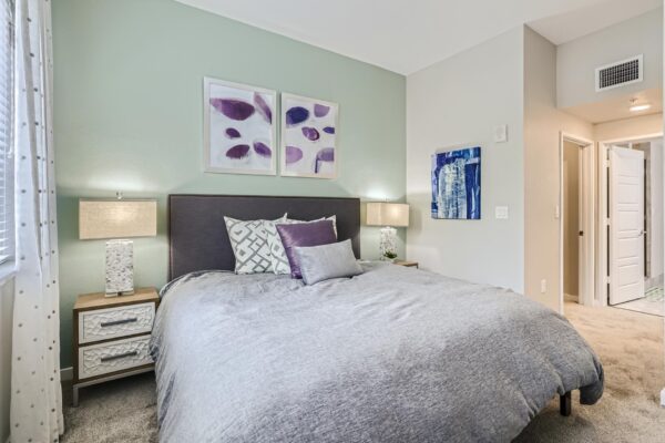 500 Ocean apartment bedroom with carpet, plush bed with headboard, bedside tables with lamps, and framed artwork.