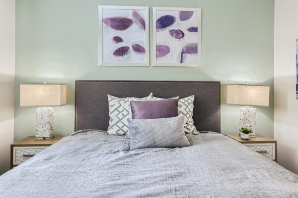 500 Ocean apartment bedroom with carpet, plush bed with headboard, bedside tables with lamps, and framed artwork.