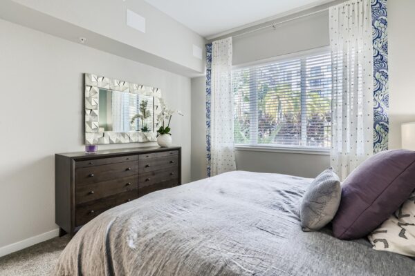 500 Ocean apartment bedroom with carpet, plush bed with headboard, dresser with vase, and framed mirror.