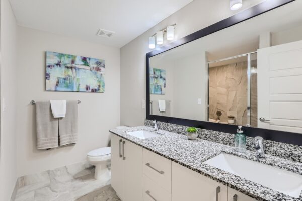 500 Ocean apartment bathroom with tile floor, white cabinets, stone counter, and framed mirror.