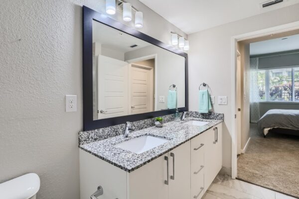 500 Ocean apartment bathroom with tile floor, white cabinets, stone counter, and framed mirror.