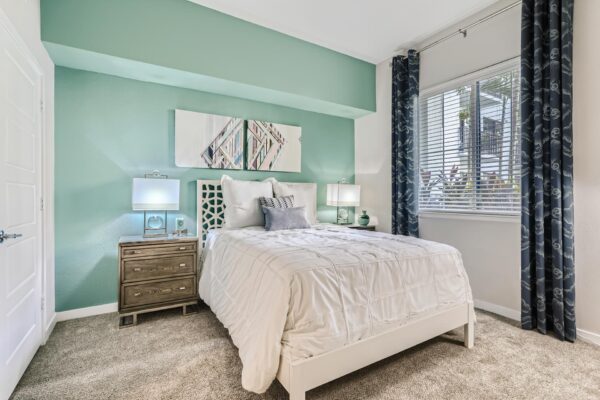 500 Ocean apartment bedroom with carpet, plush bed with headboard, bedside tables with lamps, and artwork.