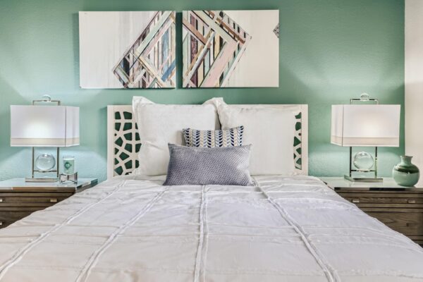 500 Ocean apartment bedroom with carpet, plush bed with headboard, bedside tables with lamps, and artwork.