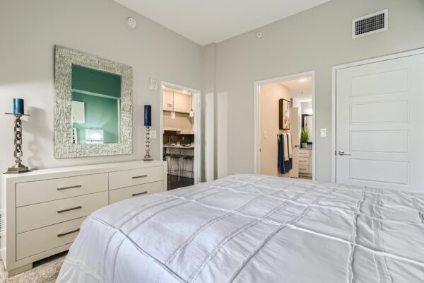 500 Ocean apartment bedroom with carpet, plush bed with headboard, dresser with candles, and framed mirror.