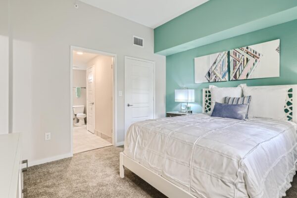 500 Ocean apartment bedroom with carpet, plush bed with headboard, bedside tables with lamps, and artwork.