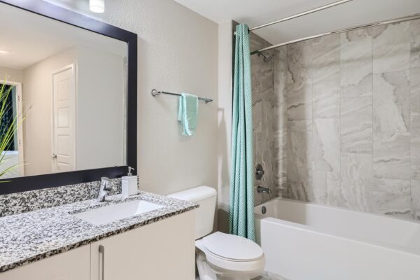 500 Ocean apartment bathroom with white cabinets, stone counters, framed mirror, and tiled shower tub.