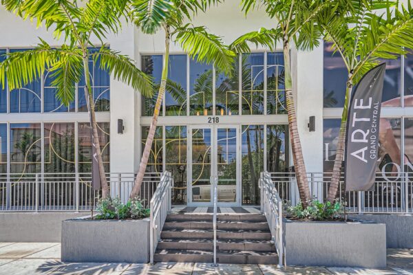 Arte Grand Central apartments leasing center entrance with large glass doors and palm trees.