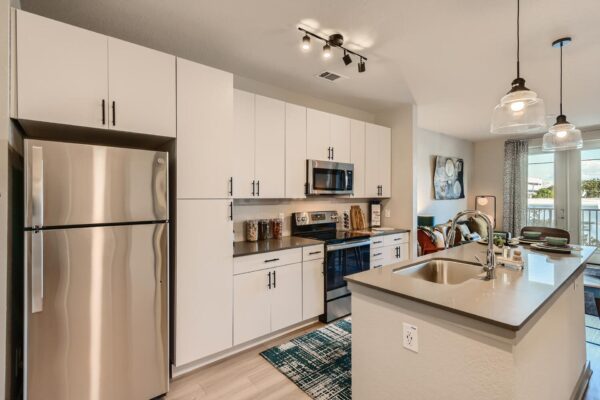 Arte St. Pete apartments kitchen with stainless steel appliances, backsplash, white cabinets, and wood-style floors.