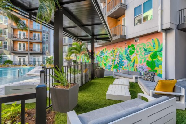Arte St. Pete apartments pool area with lounge chairs, palm trees, outdoor seating, grills, outdoor games, and apartment balconies.