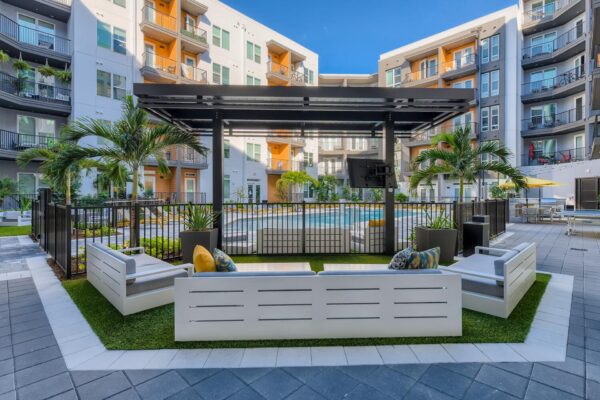 Arte St. Pete apartments pool area with lounge chairs, palm trees, outdoor seating, grills, outdoor games, and apartment balconies.