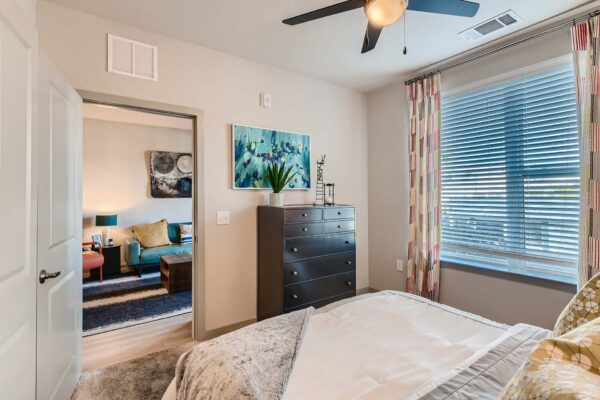 Arte St. Pete apartment bedroom with carpet, plush bed, dresser, and large window.