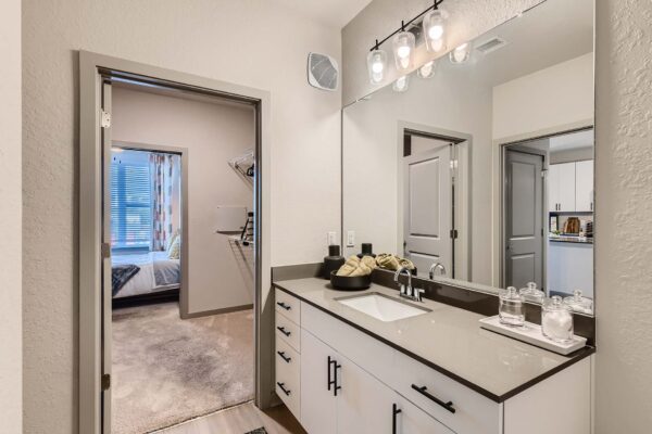 Arte St. Pete apartment bathroom with light cabinets, gray counters, and large mirror.