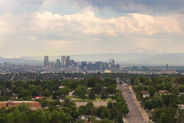 Aerial view of downtown Denver with distant mountain peaks and large clouds.
