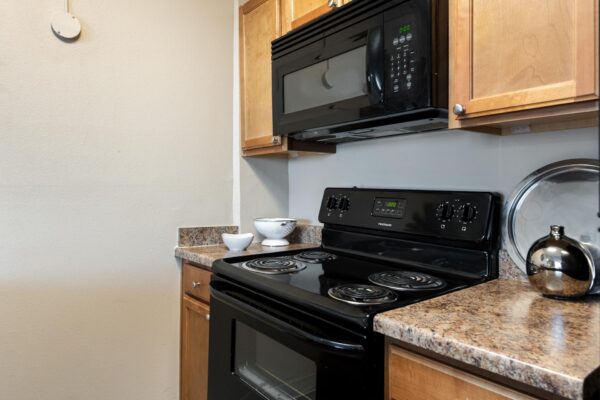Beacon House apartment kitchen with wood cabinets, tan counters, and black appliances.