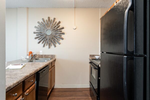Beacon House apartment kitchen with wood style floor and cabinets, tan counters, and black appliances.