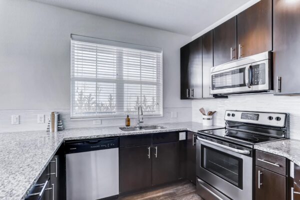 Centre Court apartment kitchen with wood style floor and cabinets, stone counters, and stainless steel appliances.