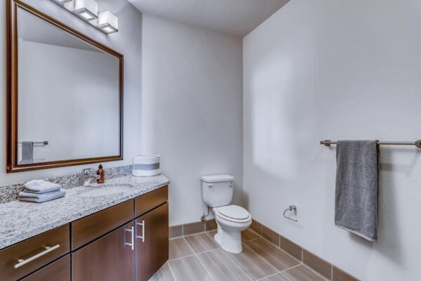 Centre Court apartment bathroom with tile floor, wood cabinets, stone counters, and framed mirror.