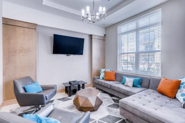 Centre Court apartments community lounge with plush sectional, leather lounge chairs, and TV.