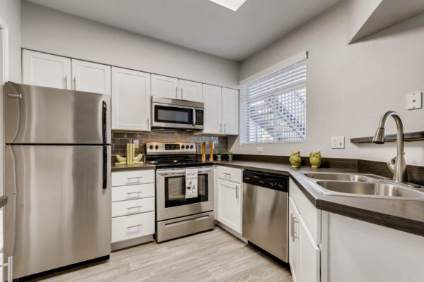 Copper Ridge apartment kitchen with wood style floor, white cabinets, dark counters, and stainless steel appliances.