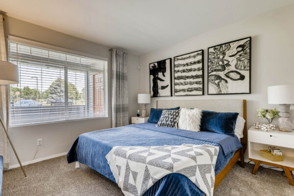 Copper Ridge apartment bedroom with carpet, plush bed with headboard, large window, and artwork.