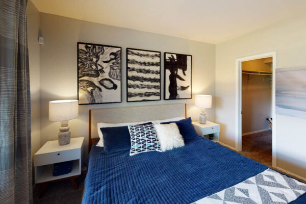 Copper Ridge apartment bedroom with plush bed, bedside tables with lamps, and artwork.`