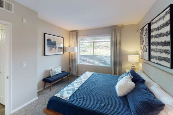 Copper Ridge apartments bedroom with carpet, plush bed with headboard, large windows, and artwork.