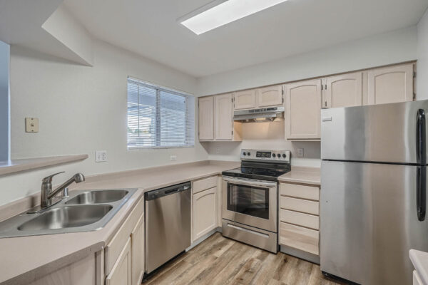 Copper Ridge apartment kitchen with wood style floor, tan cabinets and counters, and stainless steel appliances.