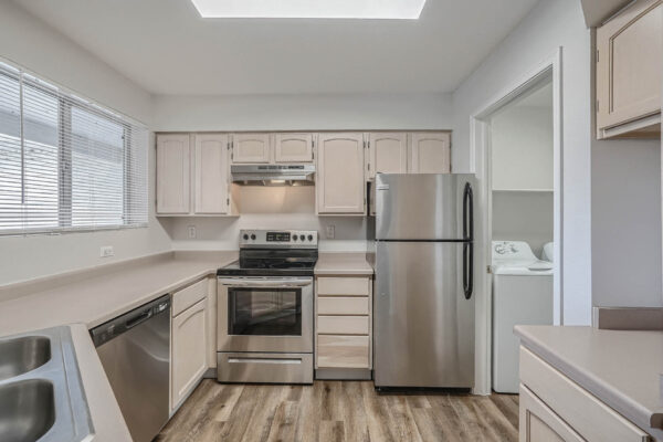 Copper Ridge apartment kitchen with wood style floor, tan cabinets and counters, and stainless steel appliances.