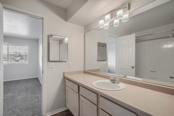 Copper Ridge apartment bathroom with tan cabinets and counters, large mirror, and medicine cabinet.