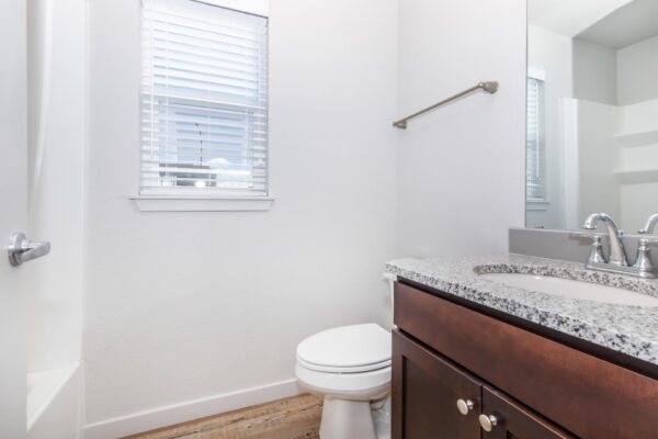 Cottages at Jet Wing apartment bathroom with wood style floors and cabinets, stone counters, and large mirror.