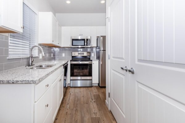 Cottages at Jet Wing apartment kitchen with wood style floor, white cabinets, stone counters, and stainless steel appliances.