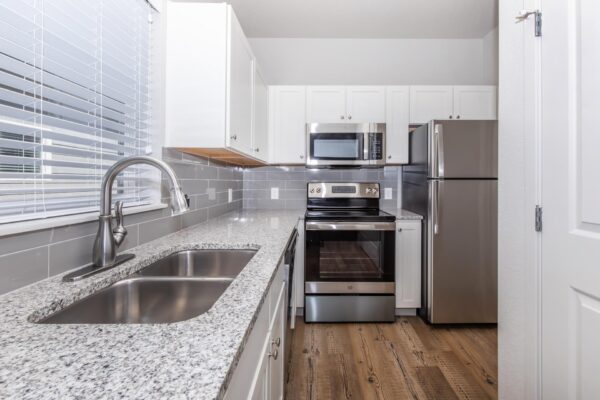 Cottages at Jet Wing apartment kitchen with wood style floor, white cabinets, stone counters, and stainless steel appliances.