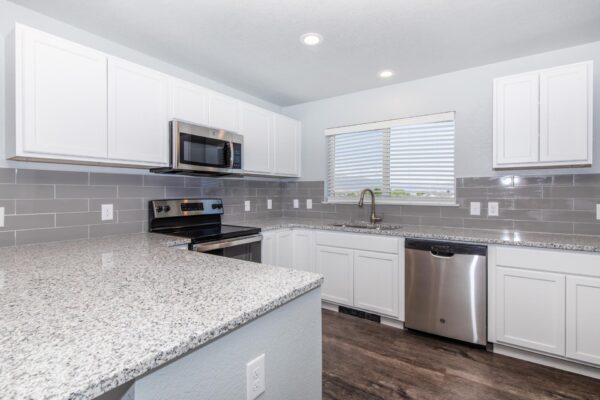 Cottages at Torin Point apartment kitchen with wood style floor, white cabinets, granite counters, and tiled backsplash.