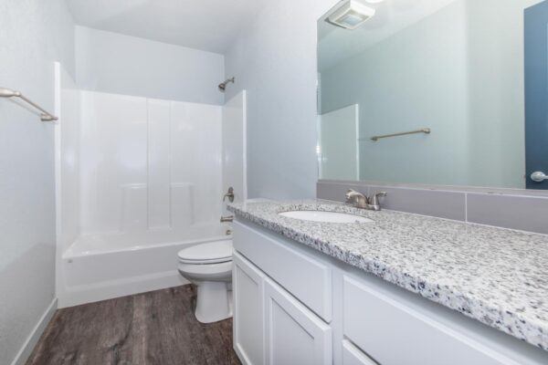 Cottages at Torin Point apartment bathroom with wood style floor, white cabinets, and stone counters.