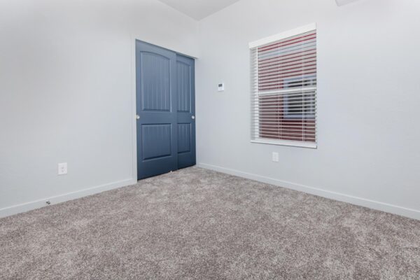 Cottages at Torin Point apartment bedroom with plush carpet, blue closet door, and large window.