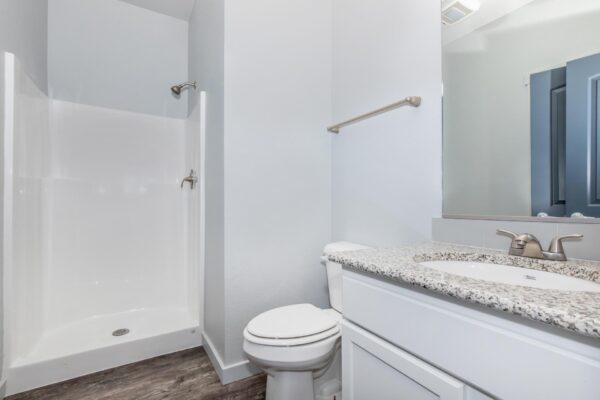Cottages at Torin Point apartment bathroom with white cabinets, granite counters, large mirror, and shower.