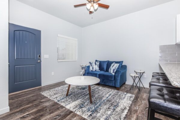 Cottages at Torin Point apartment living room with wood style floor, plush seating, blue door, and ceiling fan.