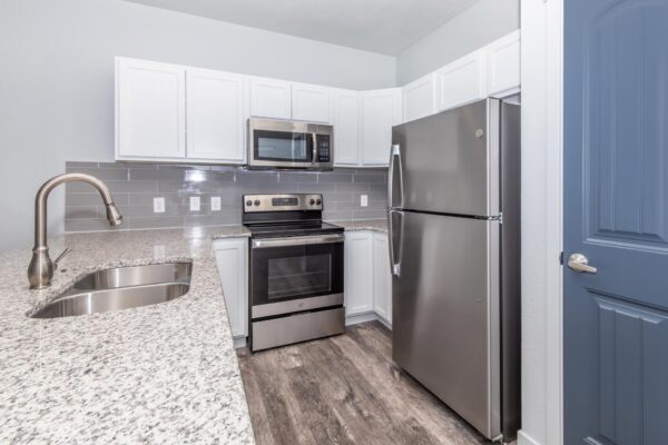 Cottages at Torin Point apartment kitchen with wood style floor, white cabinets, stone counters, and stainless steel appliances.