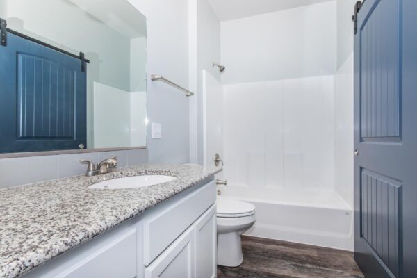 Cottages at Torin Point apartment bathroom with wood style floor, white cabinets, stone counters, and shower tub.