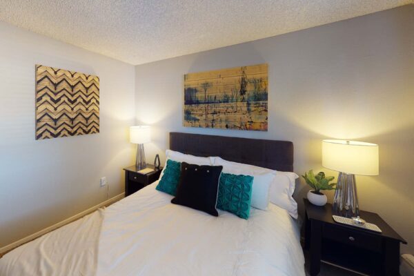 Flats at Pinecliff apartment bedroom with plush bed with headboard, bedside tables with lamps, and artwork.