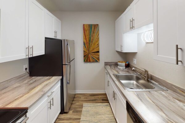 Flats at Pinecliff apartment kitchen with wood style floor, white cabinets, and stainless steel appliances.