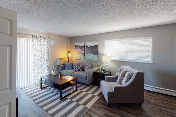 Flats at Pinecliff apartment living room with wood style floor, pattern rug, plush seating, and large windows.