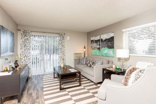 Flats at Pinecliff apartment living room with wood style floor, pattern rug, plush seating, and balcony door.