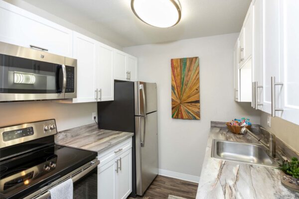 Flats at Pinecliff apartment kitchen with wood style floor, white cabinets, stainless steel appliances, and artwork.