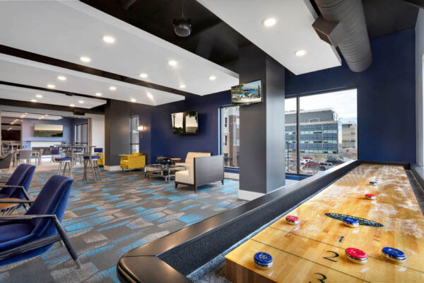 Forum Fitzsimons apartments club room with shuffleboard and plush seating.
