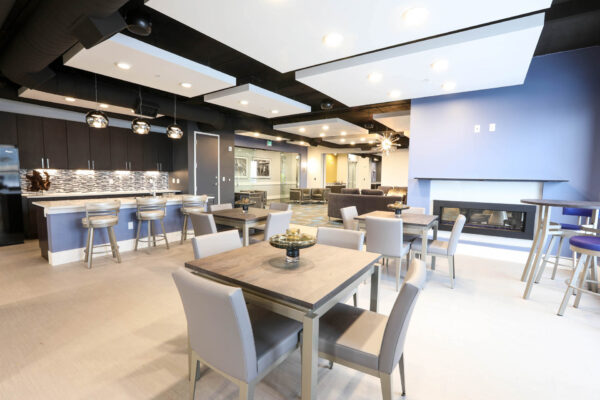 Forum Fitzsimons apartments lounge with community kitchen, dining tables, and fireplace.